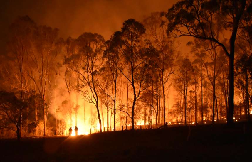 Two small, silhouetted human figures surrounded by bright yellow and orange flames, trees and smoke.