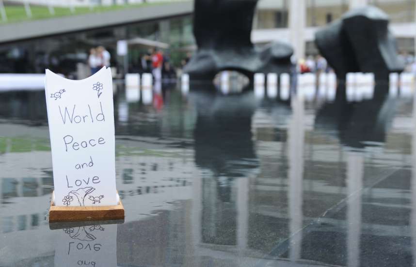 A simple lantern of paper with a wooden base with a written message reading “World Peace and Love” can be seen, floats in a still body of water, causing ripples.