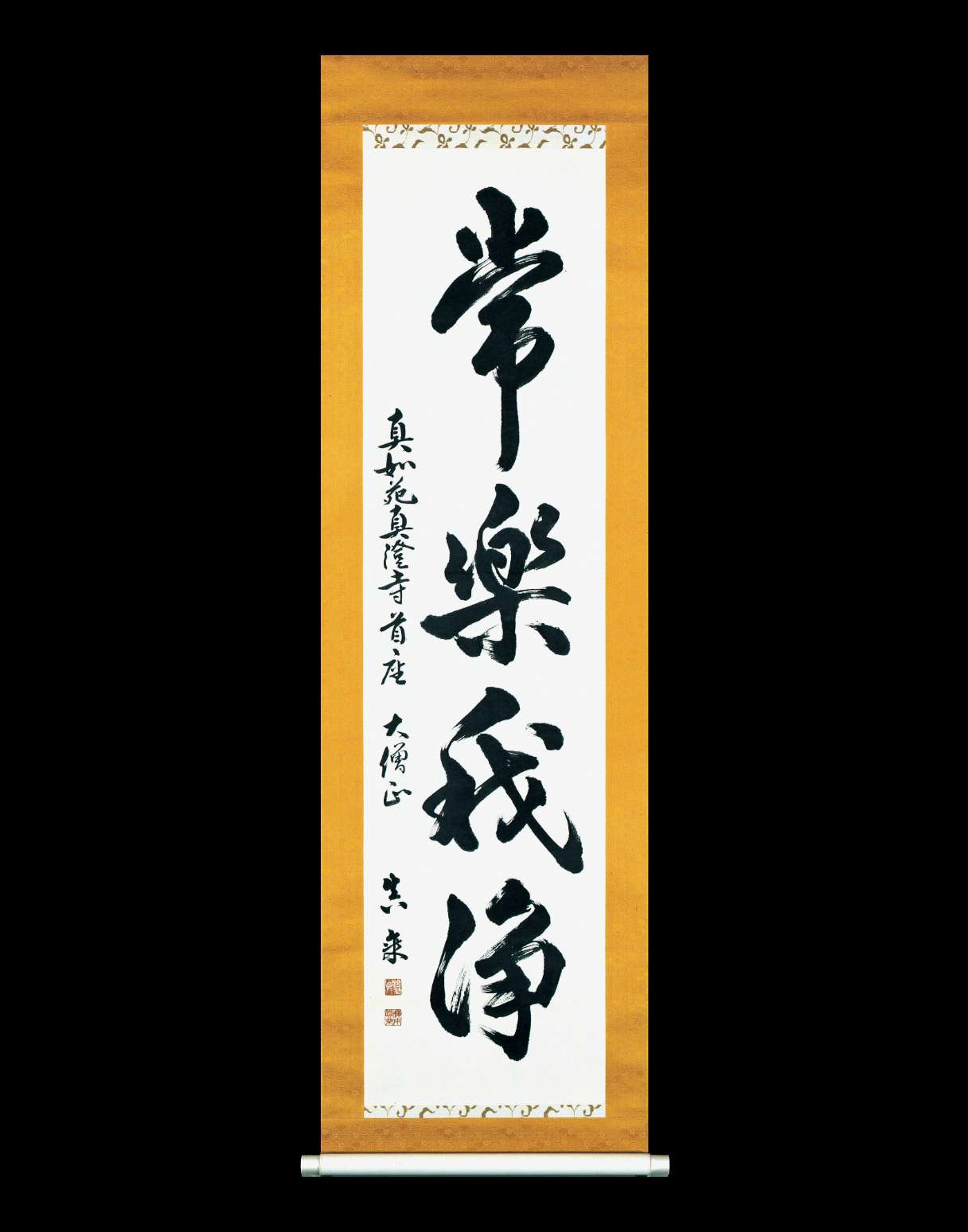 Large, bold Japanese calligraphy is written vertically on a paper scroll with an amber border, filling almost all of the space; to the left there is a vertical line of calligraphy in a smaller hand.