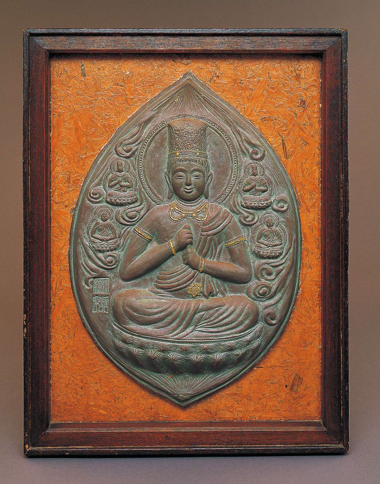 An upright almond-shaped grayish relief of a buddha wearing a tall crown sitting cross-legged, grasping his upturned left index finger with his right hand, surrounded by clouds and four smaller buddhas.