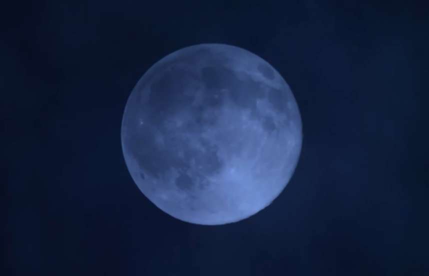 A view of a blue tinted, full moon on a black evening sky.