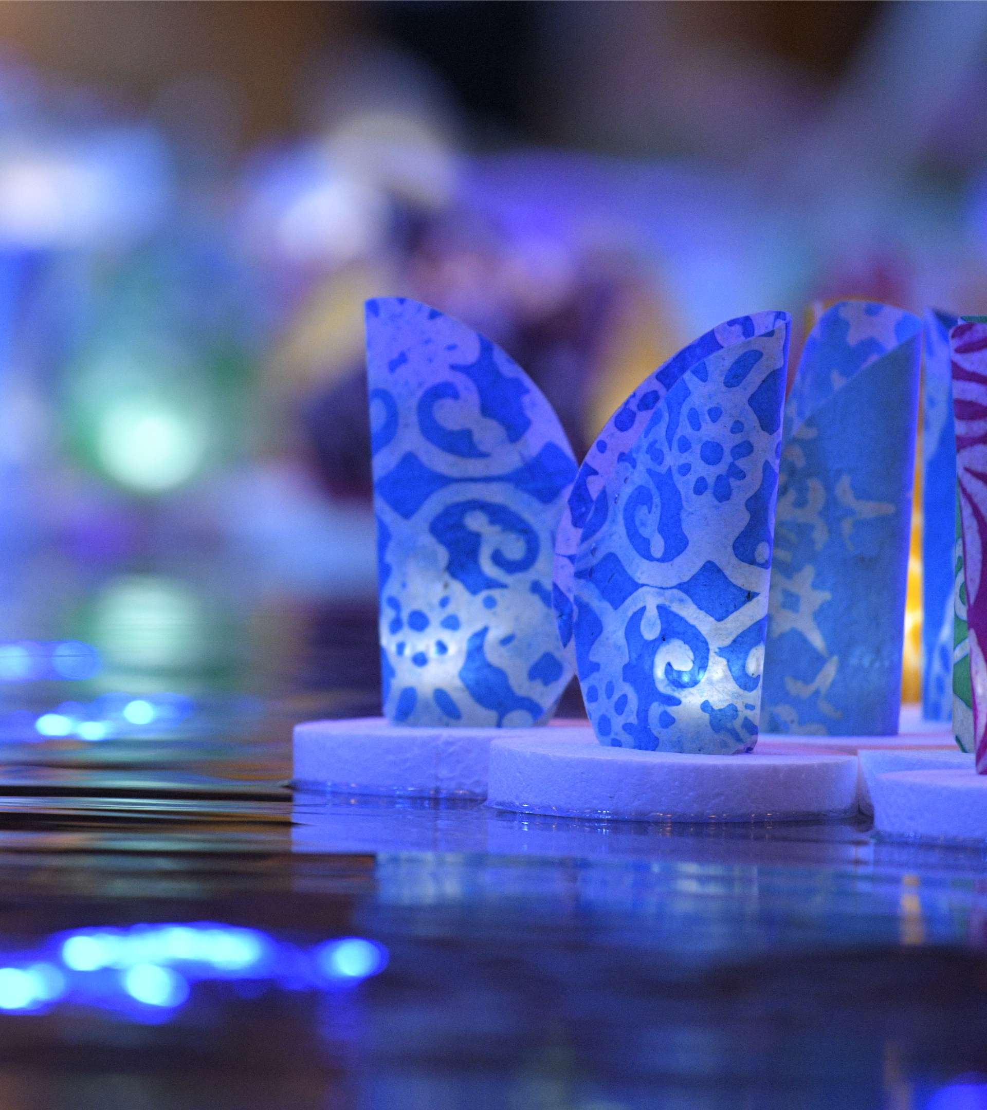 Glowing, colorful lanterns decorated with ornamental patterns float on calm water.