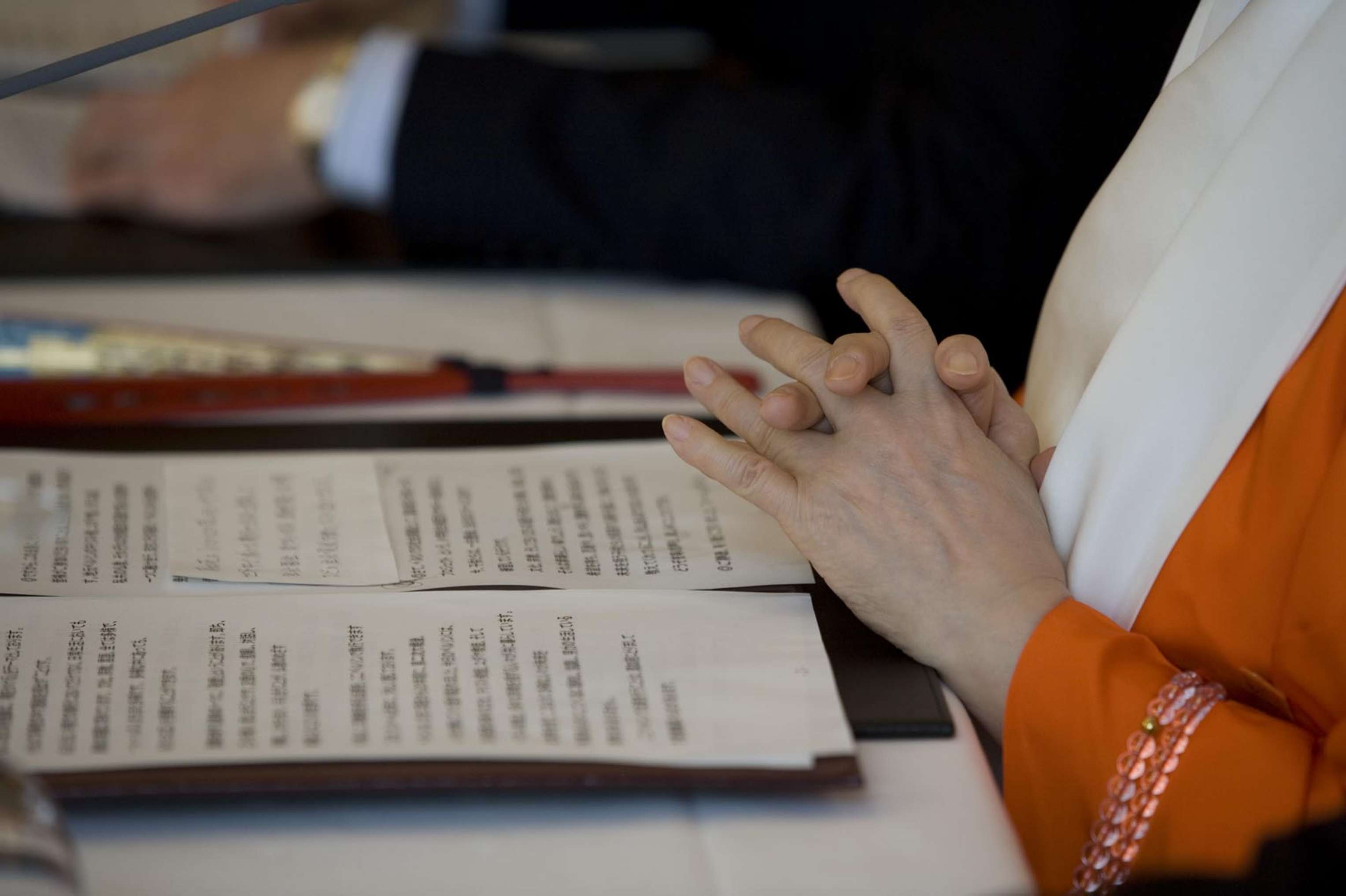 Two hands folded gently, as if in prayer, before an open text of Japanese writing.