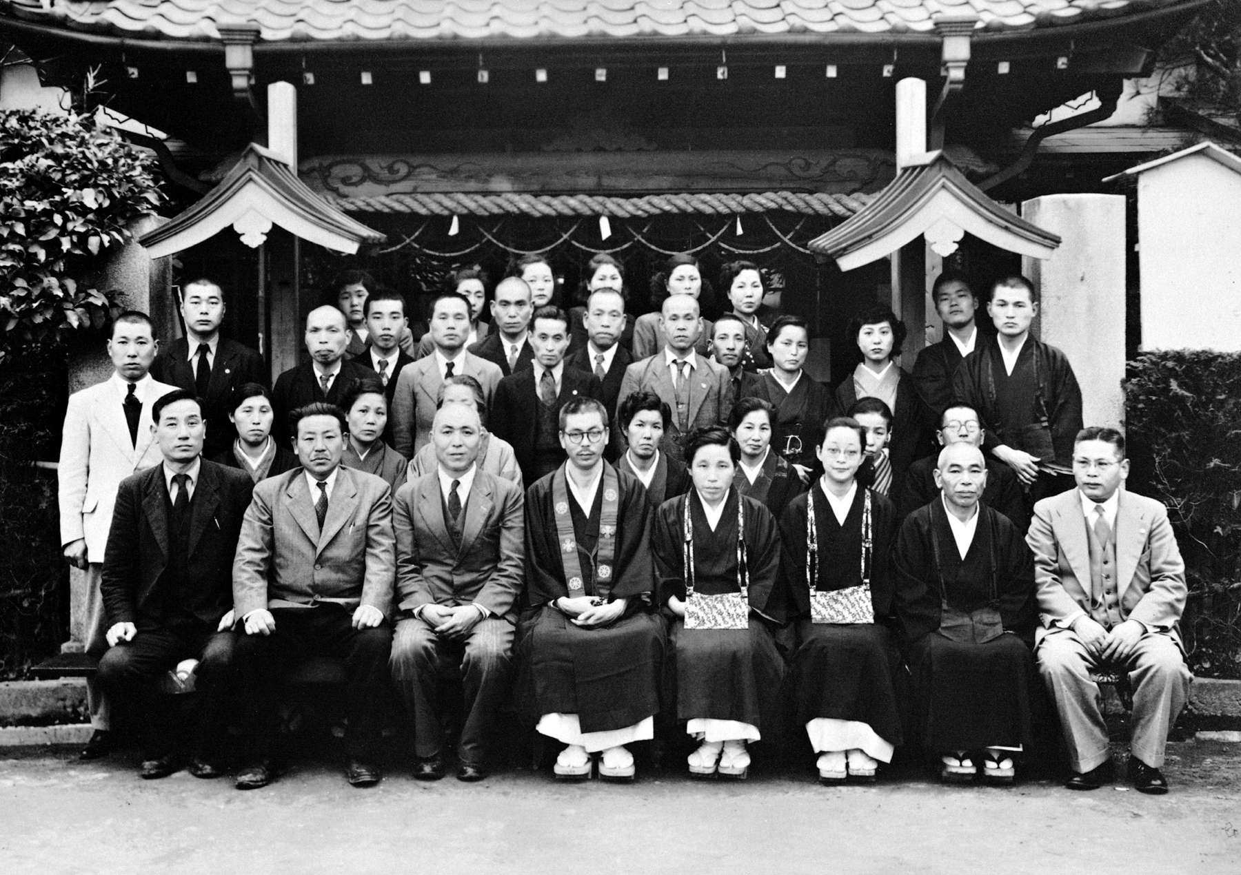 Shinjo and Tomoji, seated center, wearing priestly robes, pose for a portrait with a large, formally dressed group in front of the gate to Shinchoji temple.
