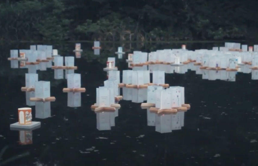 White lanterns, some with discernible writing on them, float atop wooden bases in a pond.
