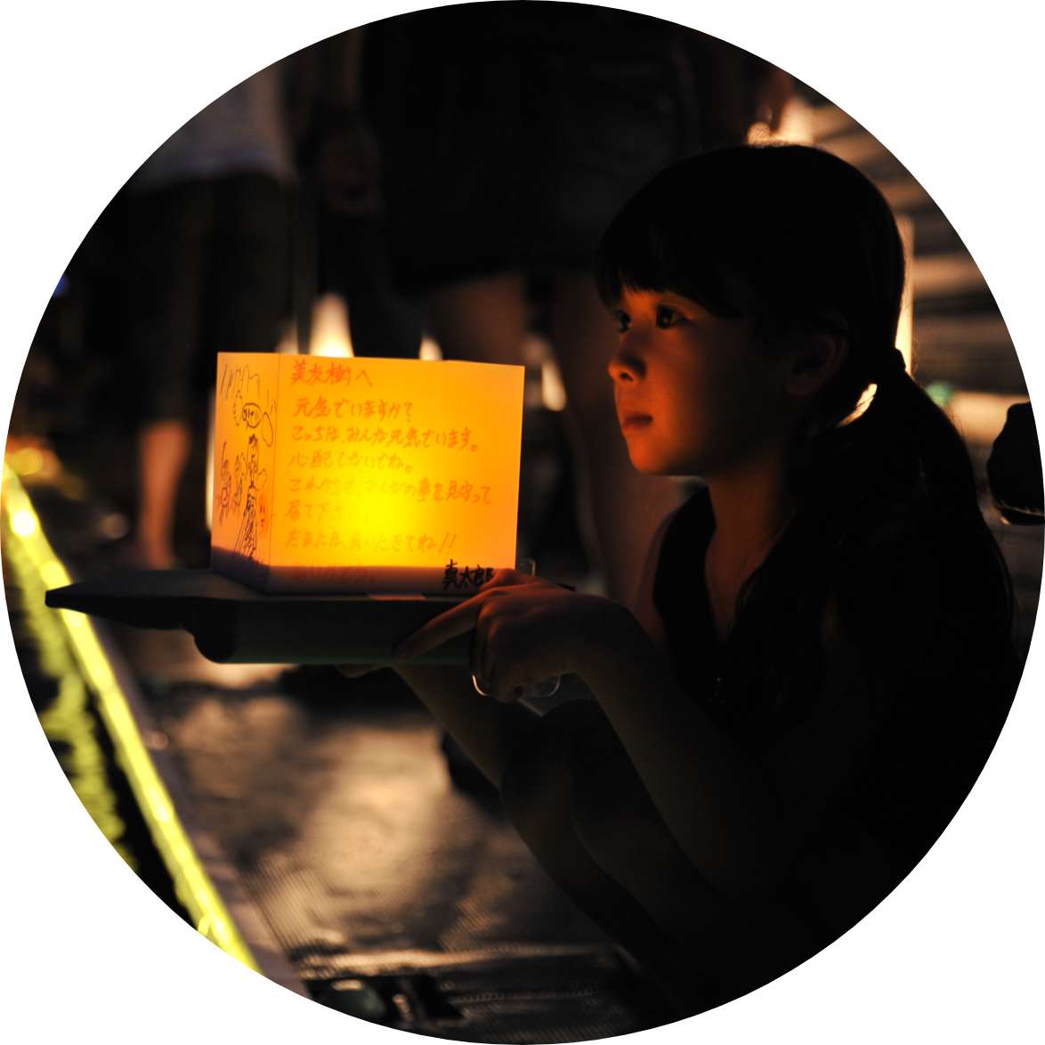 A young girl holds an illuminated lantern, the glow of which lights her face.